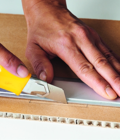 Mann durchschneidet mit einem Japanmesser einen Wabenkarton